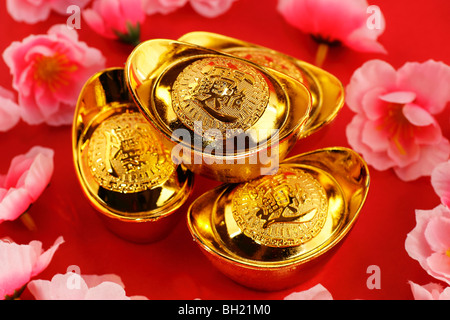 Top view of some chinese gold ingots surrounded by cherry blossoms on a red background Stock Photo