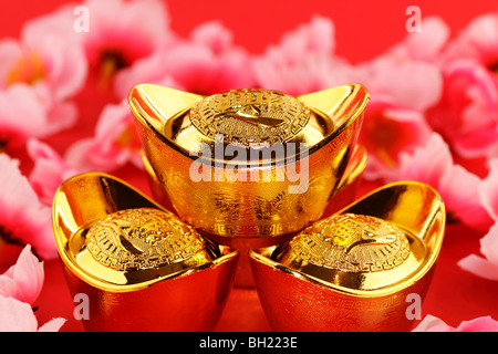 Front view of some chinese gold ingots surrounded by cherry blossoms on a red background Stock Photo