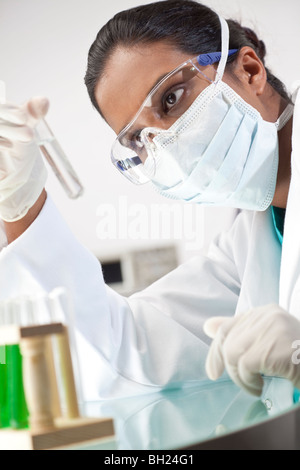 A female Asian medical or scientific researcher or doctor looking at a test tube of clear solution or liquid in a laboratory. Stock Photo