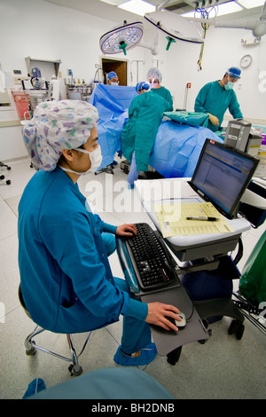 At a computer during an operation at a Southern California hospital, an Asian circulating nurse monitors patient's condition. Stock Photo