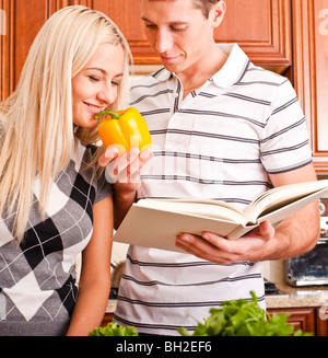 Young man with cook book holding yellow pepper for young woman to smell. Vertical shot. Stock Photo