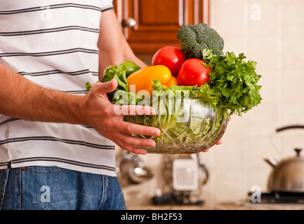 Man in striped shirt holding a bowl of vegetables in kitchen. Horizontal shot. Stock Photo