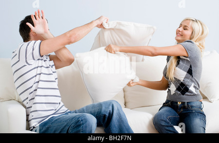 Young man holds his arm up in defense as a young woman playful hits him with a pillow. Horizontal shot. Stock Photo