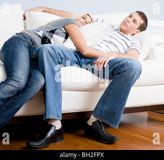 Woman snuggles up to man as they both relax quietly on a white couch. Horizontal format. Stock Photo