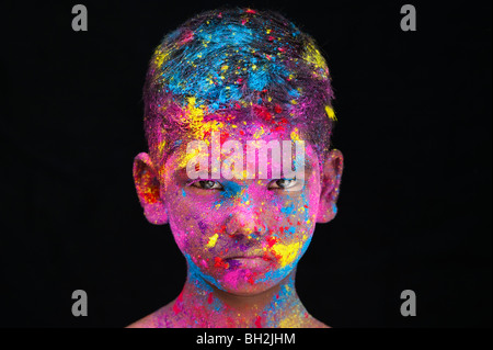 Serious young Indian boy covered in coloured powder pigment against a black background. India