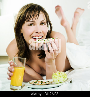 woman lying on a white bed holding orange juice Stock Photo