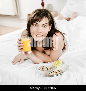 woman lying on a white bed holding orange juice Stock Photo