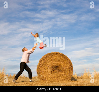 man catching boy jumping from hay bale Stock Photo