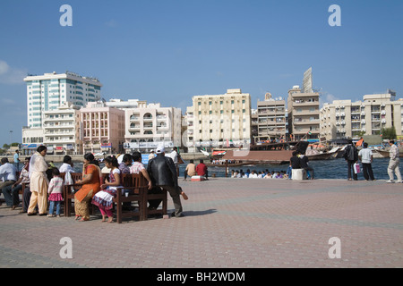 Dubai United Arab Emirates Group of Indian tourists sitting outside in the sunshine on wooden benches with views across Dubai Creek Stock Photo