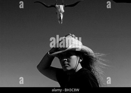 A minority woman surveys the country side while standing in front of a rustic wooden gateway as she works as a cattle rancher Stock Photo