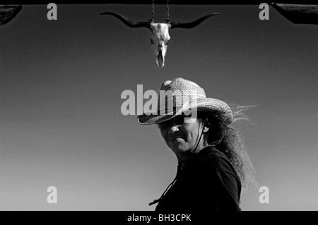 A minority woman surveys the country side while standing in front of a rustic wooden gateway as she works as a cattle rancher Stock Photo