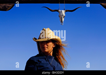 A minority woman surveys the country side while standing in front of a rustic wooden gateway as she works as a cattle rancher Stock Photo