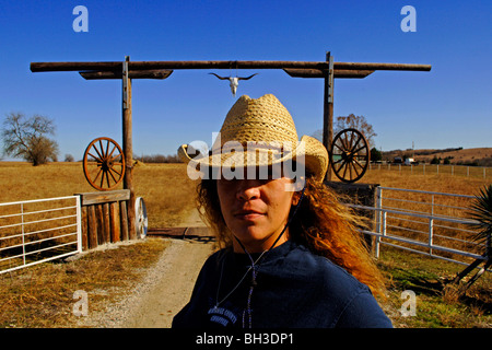 A minority woman surveys the country side while standing in front of a rustic wooden gateway as she works as a cattle rancher Stock Photo