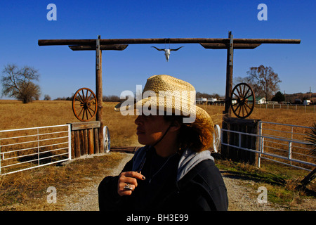 A minority woman surveys the country side while standing in front of a rustic wooden gateway as she works as a cattle rancher Stock Photo