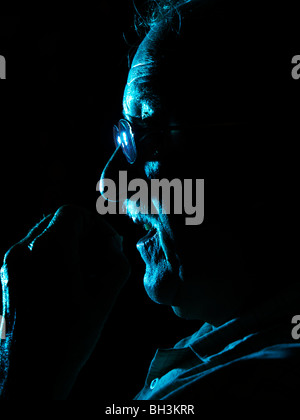 Elderly man taking tablets, hand to mouth. with dramatic blue lighting Stock Photo