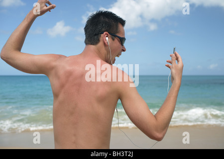 Young man listening to music on an MP3 player and singing on a deserted tropical beach Stock Photo