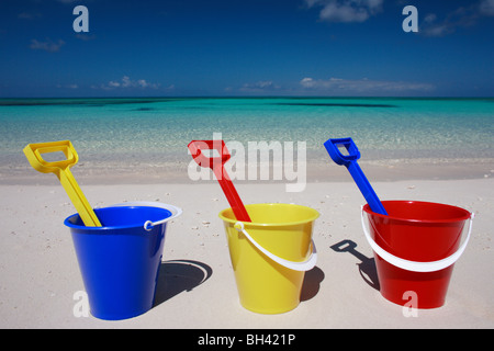 Three toy buckets and spades in a line on a tropical beach Stock Photo