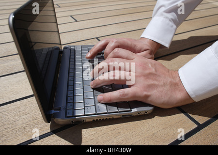 A man's hands working on a netbook computer on a wooden deck Stock Photo