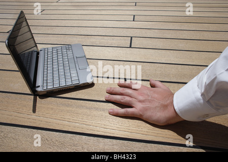 A man's hand resting next to a netbook computer on a wooden deck Stock Photo