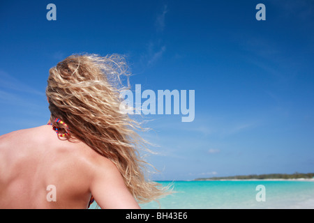 A young woman standing on a deserted tropical beach with her hair blowing in the breeze Stock Photo