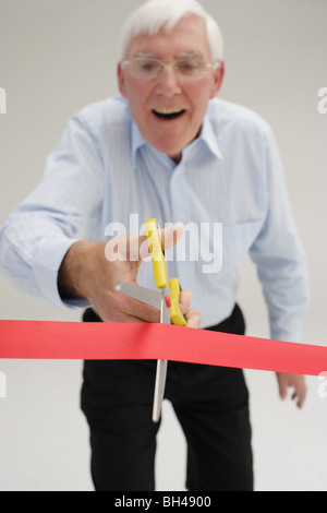 Senior businessman about to cut through a red tape, laughing Stock Photo