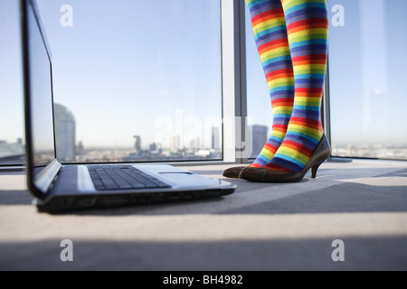 A woman's legs wearing multi colored striped stockings standing next to a laptop computer in an office Stock Photo