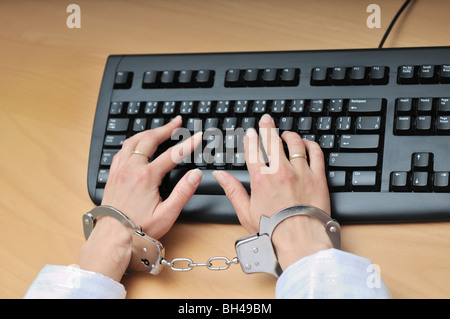 Hands tied with handcuffs typing on keyboard - crime or workaholic concept. Stock Photo