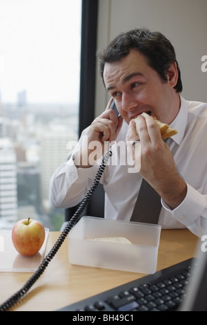 Businessman eating his lunch whilst on the telephone at an office desk Stock Photo