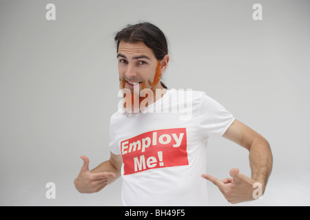 A young man pointing to his t-shirt with the message 'Employ Me!' printed over it, smiling Stock Photo
