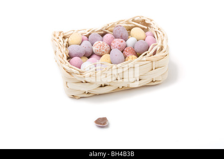 Candy covered small chocolate easter eggs in basket concept isolated against white.