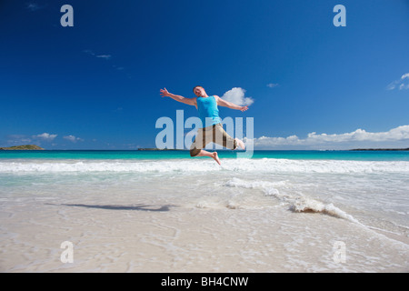 Young man leaping in the air on a deserted tropical beach, smiling Stock Photo