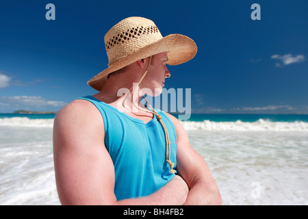 Young man wearing a straw hat looking towards the sea on a tropical beach Stock Photo