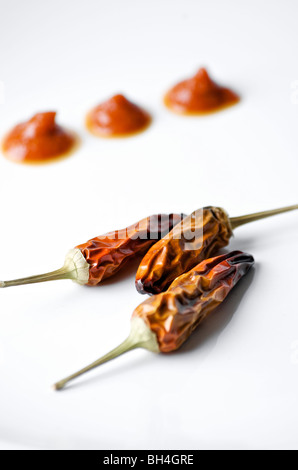 Three dried whole chili pepper and drops of red sauce against white background, Otterburn Park, Quebec Stock Photo