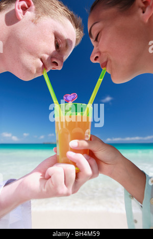 Young couple sharing a drink from a single tropical cocktail on the beach Stock Photo