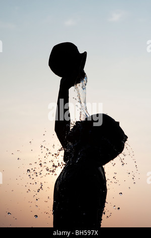 Indian boy pouring water on himself from a clay pot silhouette. Andhra Pradesh. India Stock Photo