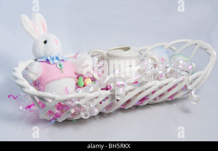 This Easter still life has a glass white lattice basket with a bunny, candy, ribbon and watering can on a light background. Stock Photo