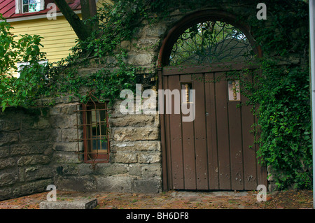 Ivy covered stone wall with window and double wooden doors with ironwork arch above  in St Augustine Florida Stock Photo
