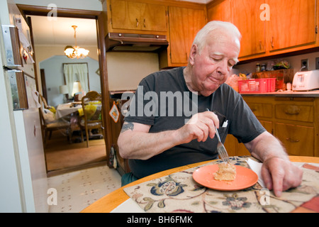 Elderly retired senior man sitting at home in his kitchen and eating. Stock Photo