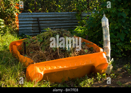 Compost heap on an allotment plot, also showing stack of cut down plastic bottles used to protect young plants Stock Photo