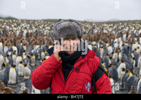 Man using satellite phone in Antarctica with a large colony of king penguins in the background Stock Photo