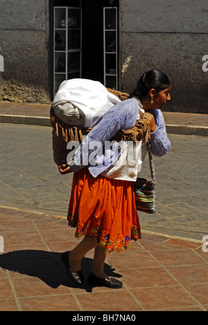 Ecuador, Cuenca, full length of an indigenous woman carrying a full bag on her back, wearing a colorful traditional skirt and w Stock Photo
