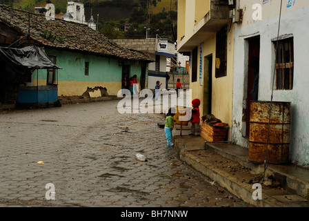 Ecuador, Latacunga, street scene in an village with rundown one storey houses and two small children playing by a yellow public Stock Photo