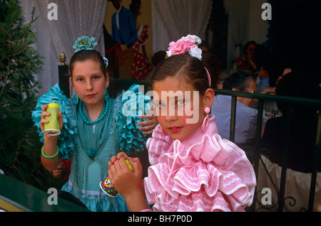 Two young flamenco-dressed sisters drink outside a caseta (marquee) during the Spring Feria in Seville. Stock Photo