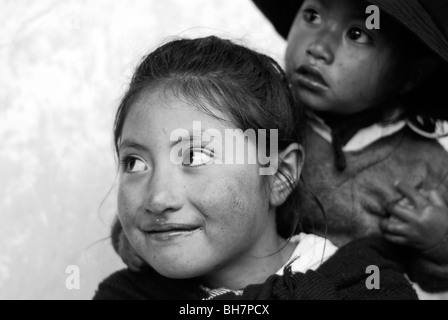 Ecuador, Latacunga, close-up of a girl ith her big bright brown eyes and smiling, her cheeks burnt by the sun, w/ baby sister Stock Photo