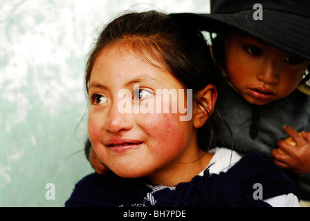 Ecuador, Latacunga, close-up of a girl ith her big bright brown eyes and smiling, her cheeks burnt by the sun, w/ baby sister Stock Photo