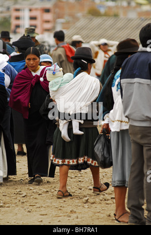 Ecuador, Otavalo, rear view of a mother wearing traditional indigenous clothes carrying a baby girl on her back Stock Photo