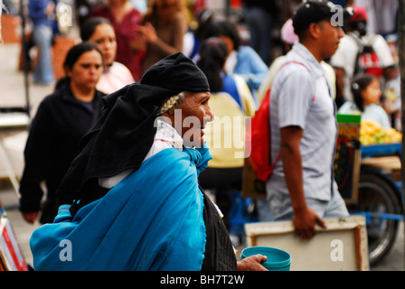 Ecuador, Otavalo, rear view of a senior woman begging in the market holding a blue plastic pot, a blue fabric wrapped around her Stock Photo