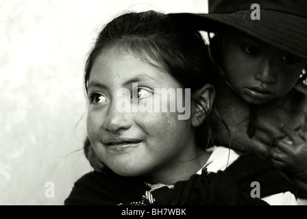 Ecuador, Latacunga, close-up of a girl ith her big bright brown eyes and smiling, her cheeks burnt by the sun, w/ baby sister Stock Photo