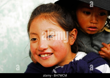 Ecuador, Latacunga, close-up of a girl ith her big bright brown eyes and smiling, her cheeks burnt by the sun, w/ baby sister Stock Photo