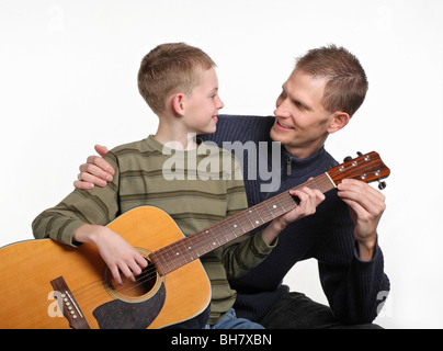 mid-adult father smiling and teaching elemetary age son how to play guitar Stock Photo
